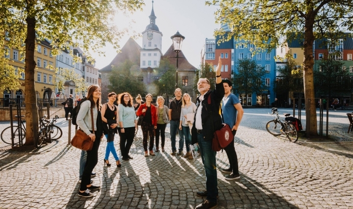 Eine Gruppe steht zu einem Stadtrundgang auf dem Marktplatz in Jena, im Hintergrund ist das Rathaus zu sehen
