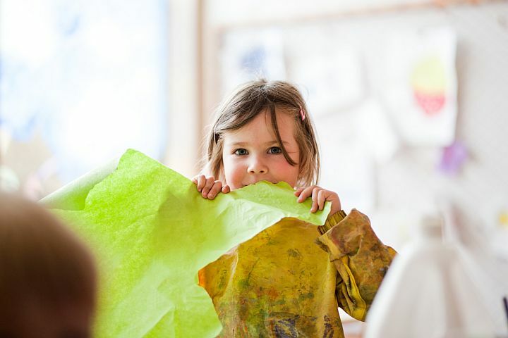 Kinder bastelt mit Papier und schaut glücklich aus