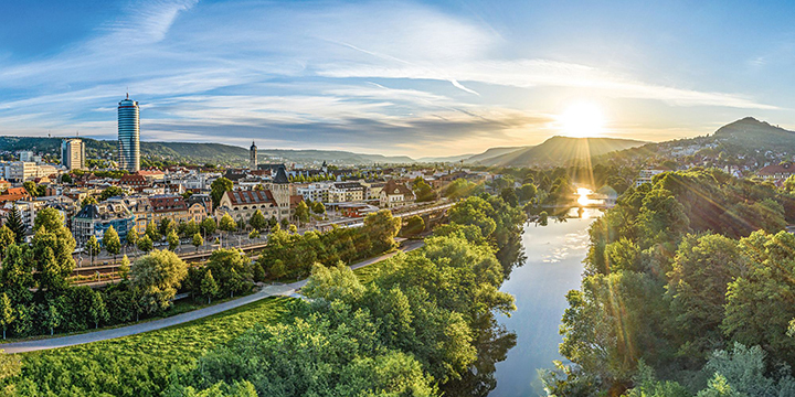 Blick auf Jena, mitten im Grünen, mit der Saale rechts durchs Bild fließend, bei Sonnenaufgang