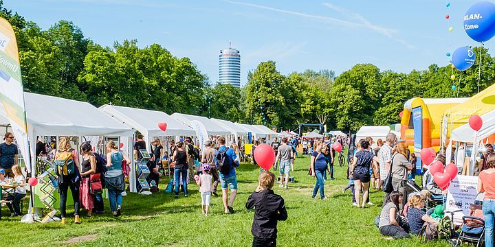 Dein Tag im Paradies, Paradieswiese mit bunten Ständen und Menschen