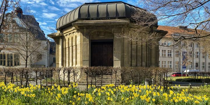 Das Ernst-Abbe-Denkmal zu Ostern, es blühe viele Osterglocken, im Hintergrund das Volkshaus Jena  ©JenaKultur, K. Schulz