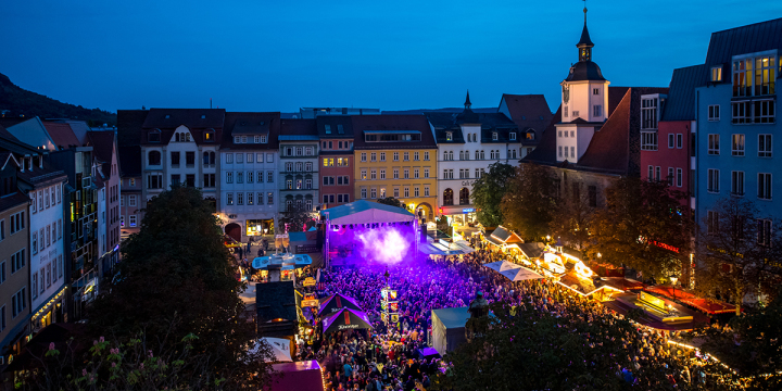 Der Marktplatz im Herzen Jena zum Jenaer Altstadtfest, voller Menschen, eine Bühne, am Abend, Stände und Licht.  ©JenaKultur, C. Häcker