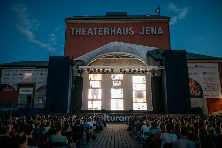 Bühne mit Leinwand, auf der ein Film läuft, und Publikum in den Sitzreihen davor bei der Kulturarena 2022 