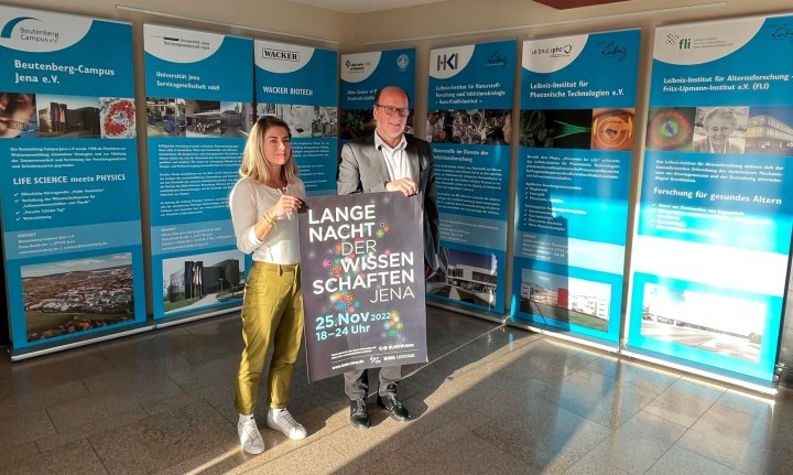 Anna Fuhlbrügge und Prof. Dr. Peter Zipfel halten ein Plakat der Langen Nacht der Wissenschaften Jena 2022 in die Kamera