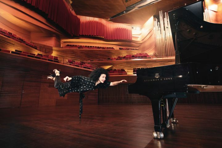 Pianistin Marianna Shirinyan in einem großen Konzertsaal schwebt mit ausgestreckter Hand auf einen Flügel zu