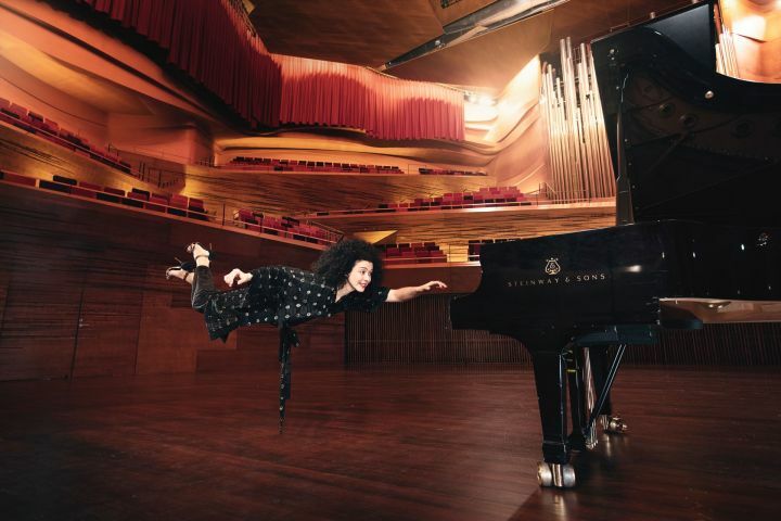 Pianistin Marianna Shirinyan in einem großen Konzertsaal schwebt mit ausgestreckter Hand auf einen Flügel zu