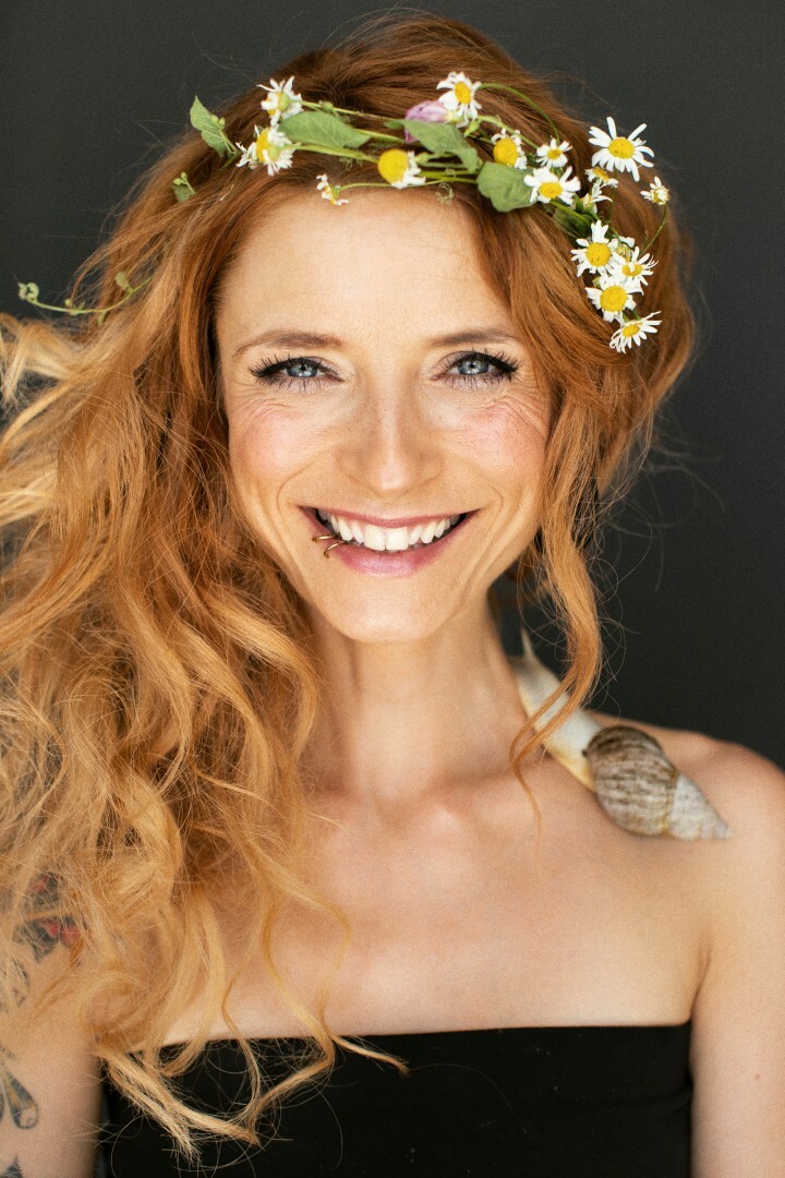 Sängerin Sarah Lesch mit Blumenkranz im Haar und einer Schnecke auf der schulter
