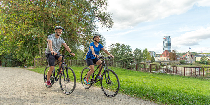 Zwei Radfahrende auf dem Saaleradweg, im Hintergrund der JenTower