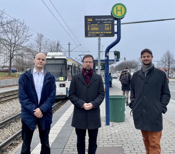 Marcus Komann, Thomas Nitzsche und Jonas Zipf an einer Straßenbahnhaltestelle mit Tram und Passanten im Hintergrund