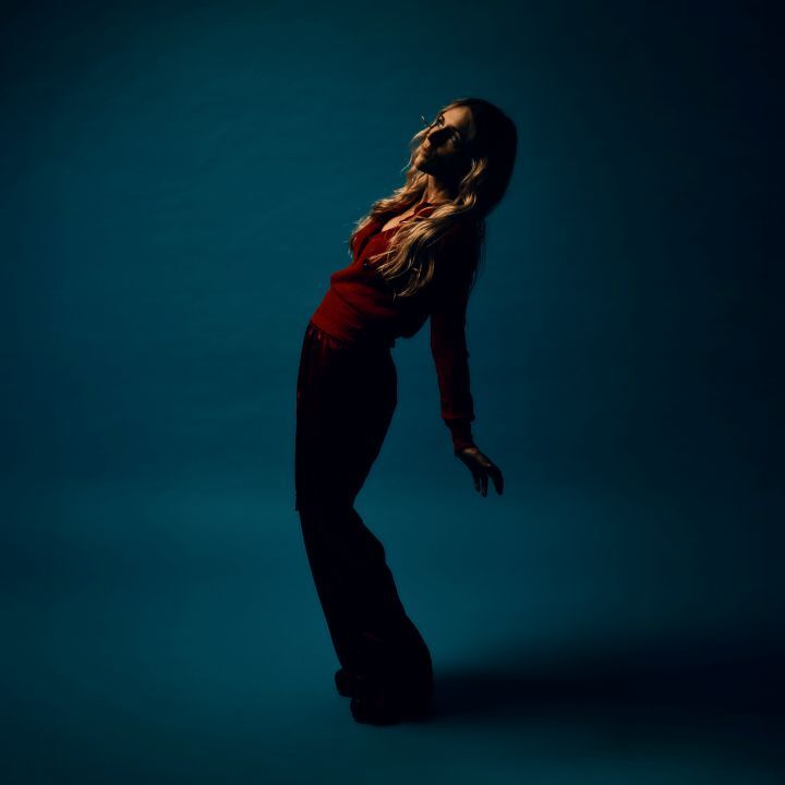 Sängerin Agnes Obel in einer Tanzpose vor türkisfarbenen Hintergrund