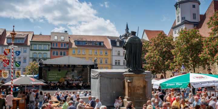 Foto von dem Jenaer Frühlingsmarkt 2024 auf dem Marktplatz mit Hanfried-Statue, Marktbühne, Publikumsbereich und historischen Gebäuden ringsums.  ©JenaKultur, R. Möbius