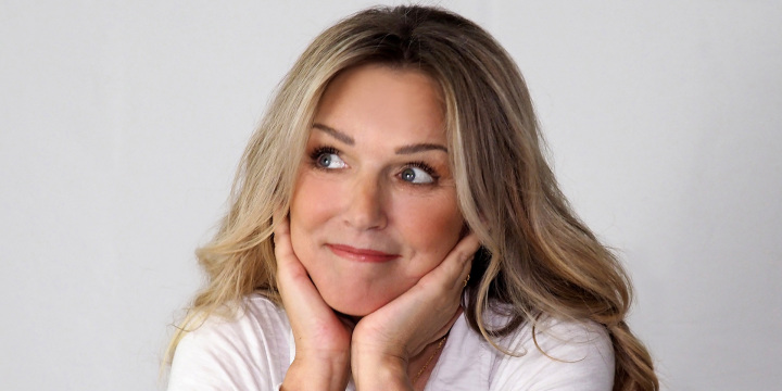 Eine Frau in weißem Oberteil und blonden Haar stützt ihren Kopf auf die Hände.