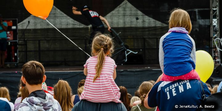 Kinder auf den Schultern ihrer Eltern vor der Bühne bei Dein Tag im Paradies mit Luftballons