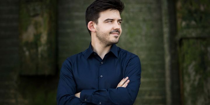 Portrait von einem Mann mit dunklem Haar und Hemd, der an der Wand steht.