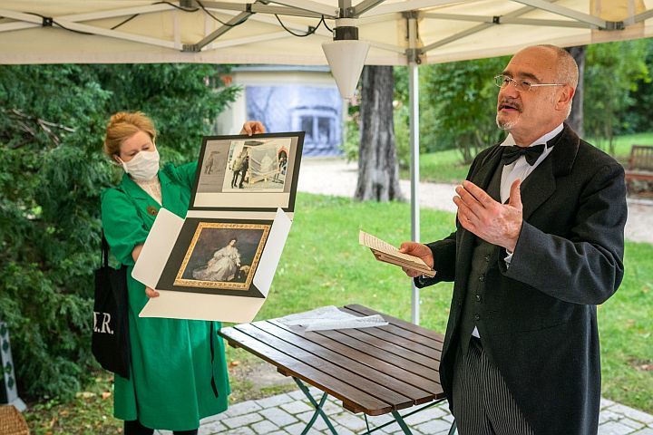 Ein Stadtführer, kostümiert, erzählt im Garten der Villa Rosenthal, eine Frau zeigt dazu historische Bilder
