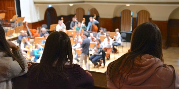 Balkonaufnahme einer Probe der Jenaer Philharmonie mit Hinterköpfen der Zuhörer:innen
