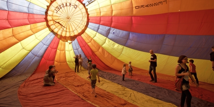 Menschen bewegen sich im Inneren eines bunten Heißluftballons. Der Schirm ist zur Hälfte mit Luft befüllt. 