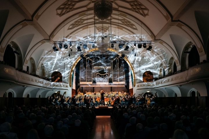 Orchester der Jenaer Philharmonie spielt auf der Bühne, an den Wände sieht man eine Lichtinstallation aus abstrakten Formen