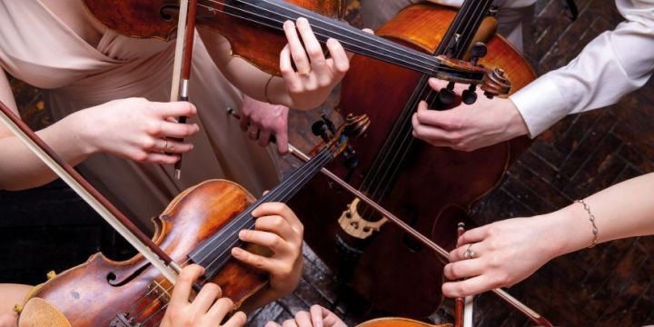 Zu sehen sind viele Hände, die jeweils Streichinstrumente spielen. Sie bilden einen Kreis. Das Foto ist von oben aufgenommen. 