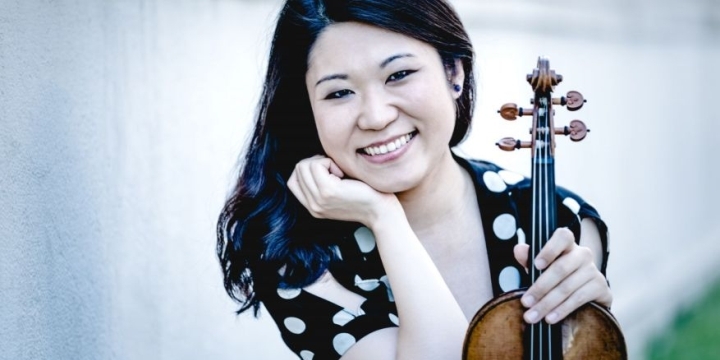 Tianwa Yang steht lächelnd mit ihrem Instrument in der Hand vor einer Mauer