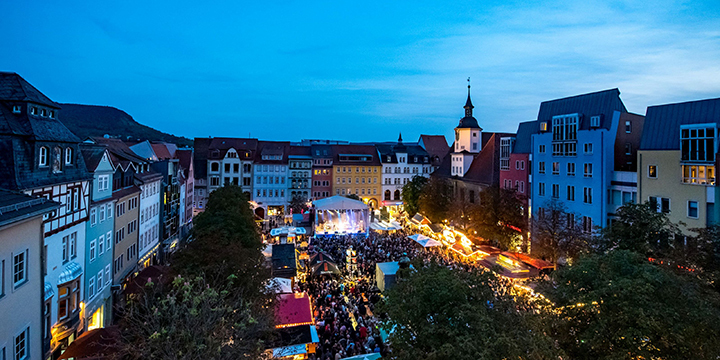 Vogelperpektive auf den historischen Marktplatz mit Bühne und Ständen des Jenaer Altstadtfestes, alles ist beleuchtet.  ©JenaKultur, C. Häcker