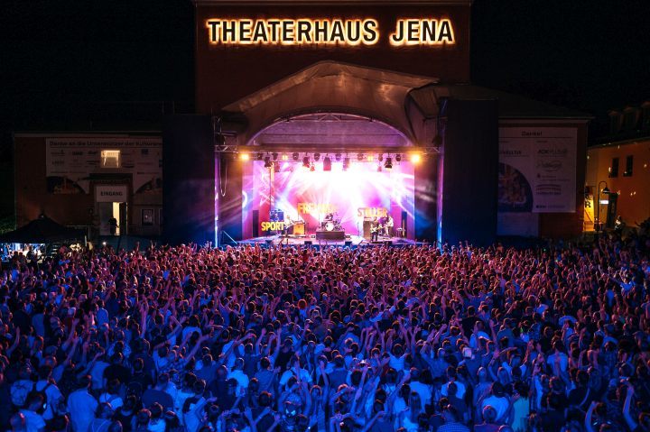 Blick auf die ausverkaufte Kulturarena Jena beim Konzert der Sportfreunde Stiller 2022, es ist dunkel, viele Menschen, bunte Bühne