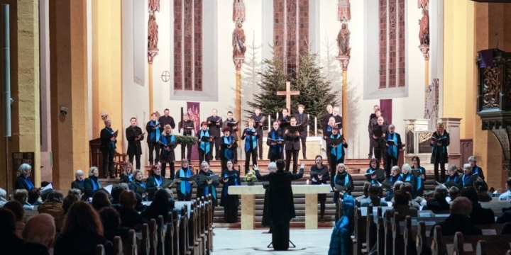 Philharmonischer Chor Jena tritt mit Dirigent in der Stadtkirche Jena auf. Man sieht die Hinterköpfe der Zuhörer:innen