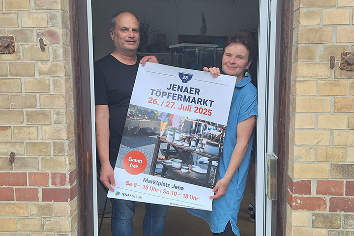 Die Töpferin Petra Lieberenz des Jenaer Töpfermarktes hält mit dem Marktmeister Oliver Klinke das Plakat für den Jenaer Töpfermarkt 2025 hoch.