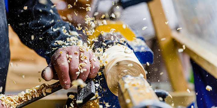 An einer Hobelmaschine wird ein Stück Holz bearbeitet, Späne fliegen