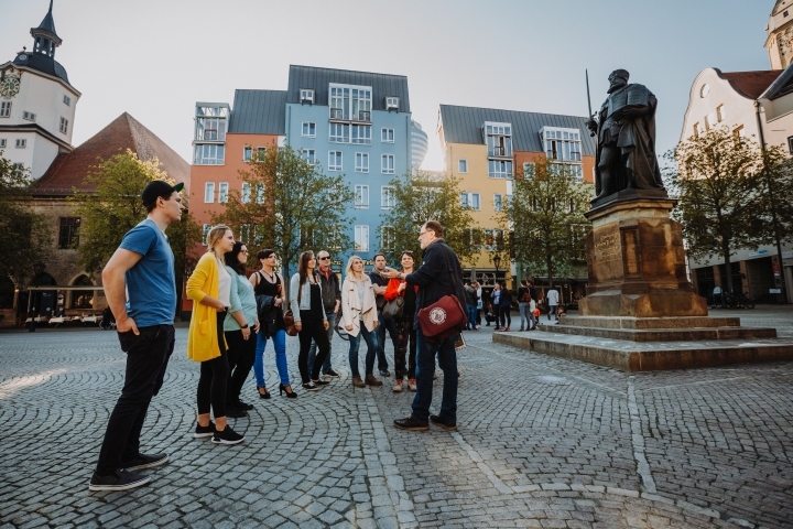 Eine Gruppe mit Stadtführer auf dem Jenaer Marktplatz vor dem Hanfried-Denkmal