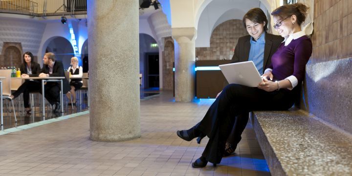 Teilnehmende einer Konferenz im Volksbad Jena abseits im Vordergrund mit einem Laptop, im Hintergrund weitere Teilnehmende an den Tischen  ©JenaKultur, A. Hub