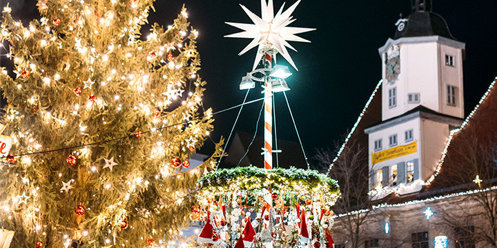 Abendstunde auf dem Jenaer Weihnachtsmarkt mit geschmückten Weihnachtsbaum, Kranz und einem weißen Rathausturm  ©JenaKultur, C. Worsch